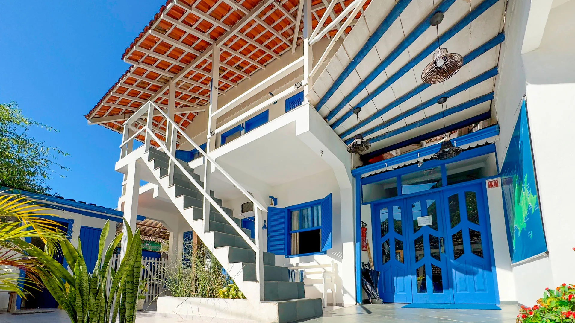 Fachada azul e branca da Pousada Costa Verde, com escada externa e telhado de telhas, na Vila do Abraão, Ilha Grande.
